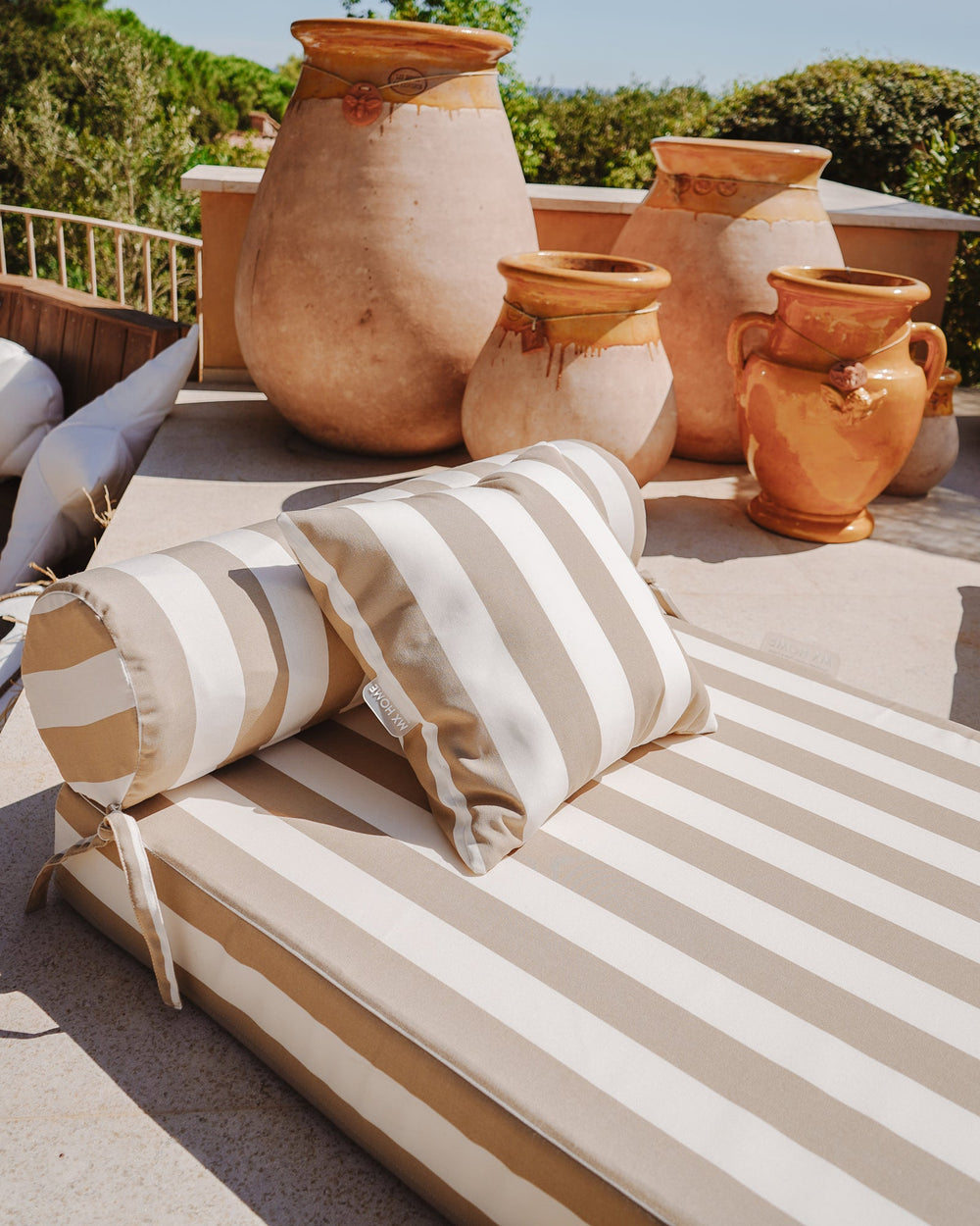 Matelas extérieur rayé beige et blanc avec têtière, utilisé sur une terrasse avec parasol.